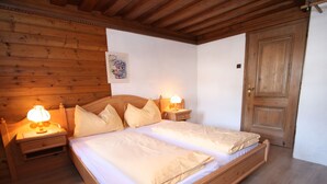 Ein hölzerner Doppelbett mit zwei Nachttischen, jeder mit einer Lampe, in einem Zimmer mit Holzwänden und einer Holztür.