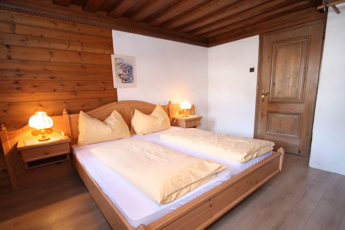 Un lit double à ossature en bois, avec deux tables de chevet, chacune équipée d’une lampe, dans une pièce aux murs et à la porte en bois.
