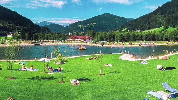 Ein Seeufer-Resort mit einem roten Gebäude, Rasenflächen und freiem Blick auf die Berge.