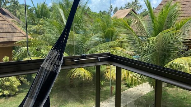 A hammock in a corner of a room with a view of a tropical garden and palm trees. - Flat 15 Eco Resort Carneiros by La Playa (Tamandaré)