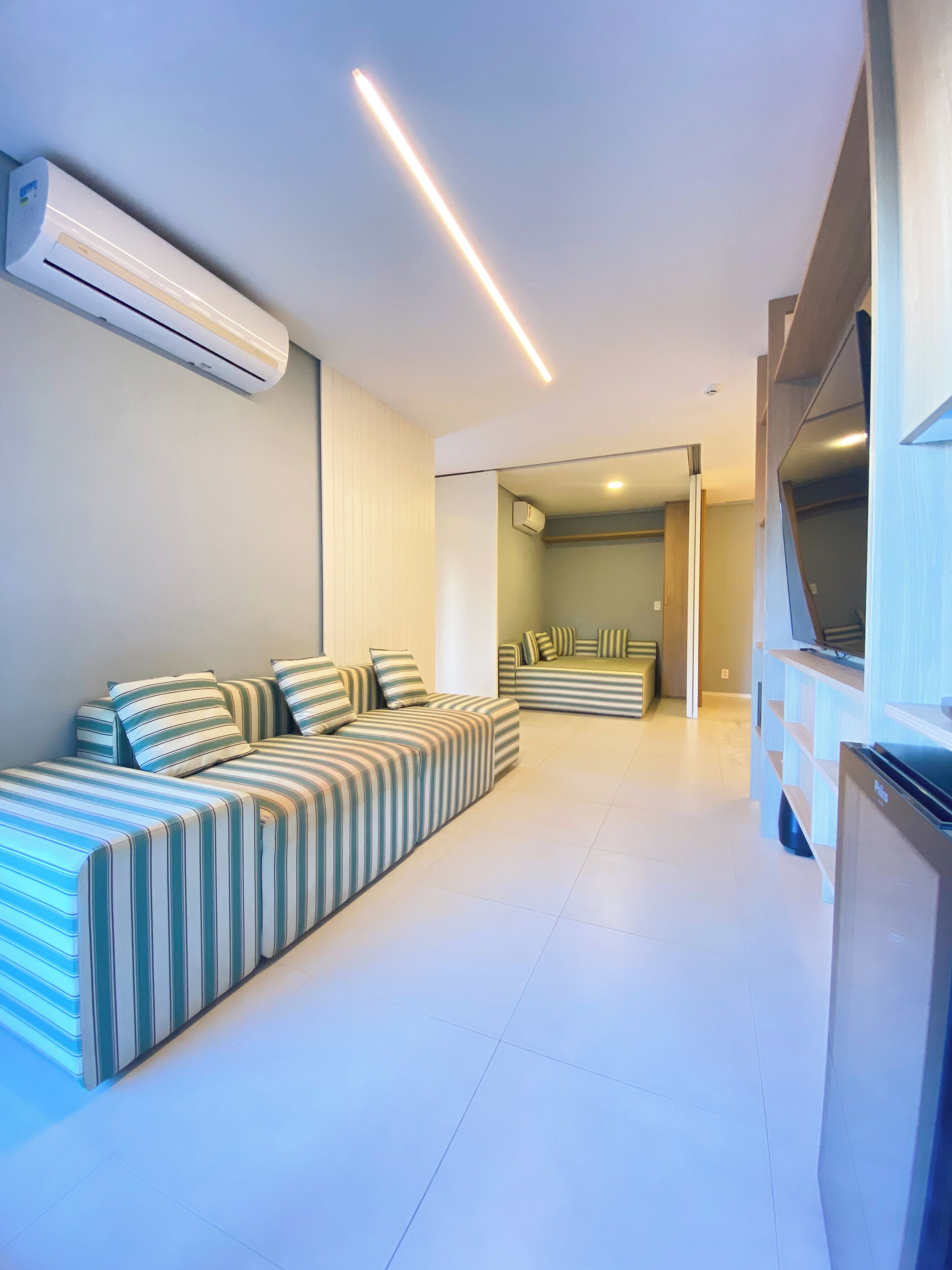 A modern living room with a sofa set, a flat-screen TV, and an air conditioning unit.