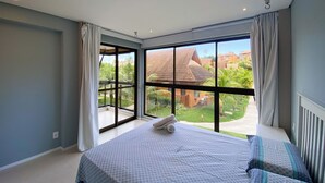A bedroom with a large window, a bed, and a view of a garden and buildings outside. - Flat 15 Eco Resort Carneiros by La Playa (Tamandaré)