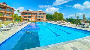A swimming pool with lounge chairs and umbrellas, surrounded by buildings with a clear sky. - Flat 15 Eco Resort Carneiros by La Playa (Tamandaré)