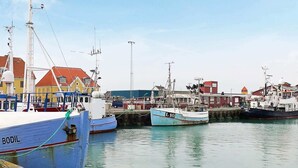 Un puerto con barcos amarrados, edificios con tejados rojos y un cielo despejado.
