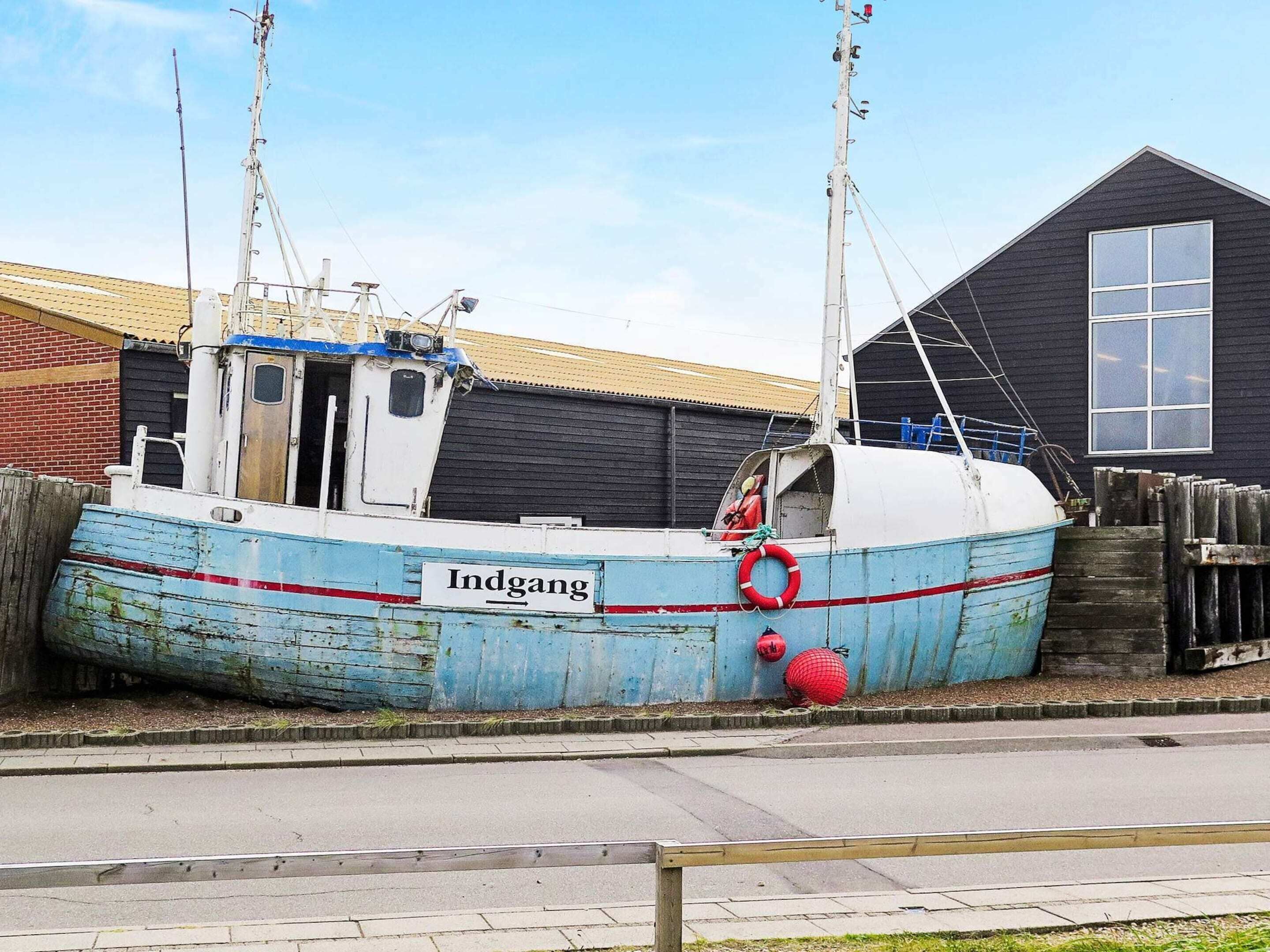 A blue and white boat named 'Indgang' docked near a building with a dark exterior and a window.