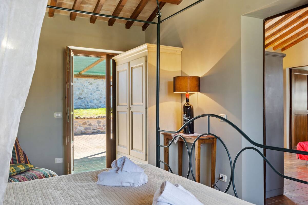 A bedroom with a bed, a bedside table with a lamp, a wardrobe, and an open door leading to an outdoor area.