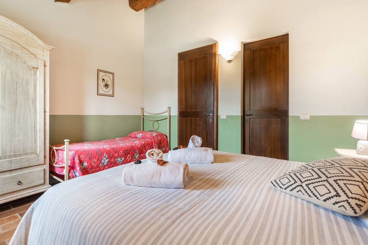 A bedroom with a large bed, two smaller beds, wooden doors, a dresser, and a framed picture on the wall.