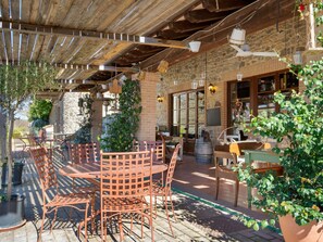Une terrasse extérieure avec une table ronde et des chaises, entourée de plantes en pot et d’un mur de pierre.