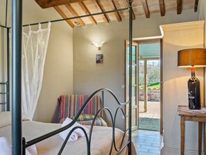 Une chambre à coucher avec un lit à baldaquin, une table de chevet avec une lampe, une fenêtre donnant sur l’extérieur et une porte menant à un patio.