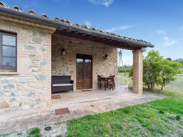A stone building with a covered patio, a wooden door, and a seating area with a chair and table. - Quaint Cottage in Citta Della Pieve With Pool (Citta della Pieve)