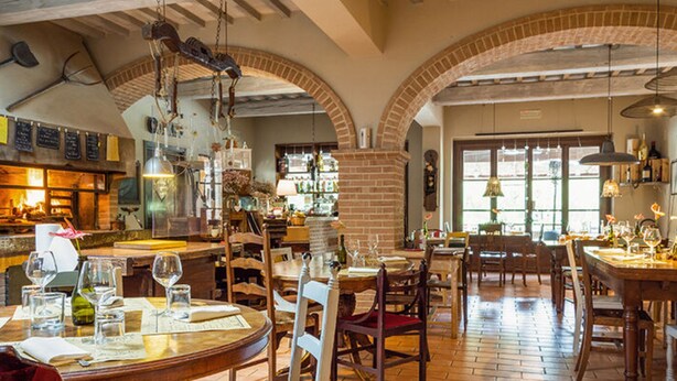 Ein Restaurant mit Backsteinbögen, Holztischen und hängenden Lampen.