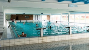 Ein Hallenbad mit mehreren Bahnen, einer sichtbaren Tiefenmarkierung und einem gefliesten Boden.