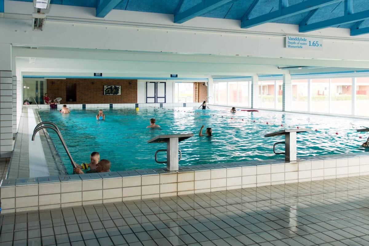 An indoor swimming pool with multiple lanes, a visible depth marker, and a tiled floor.