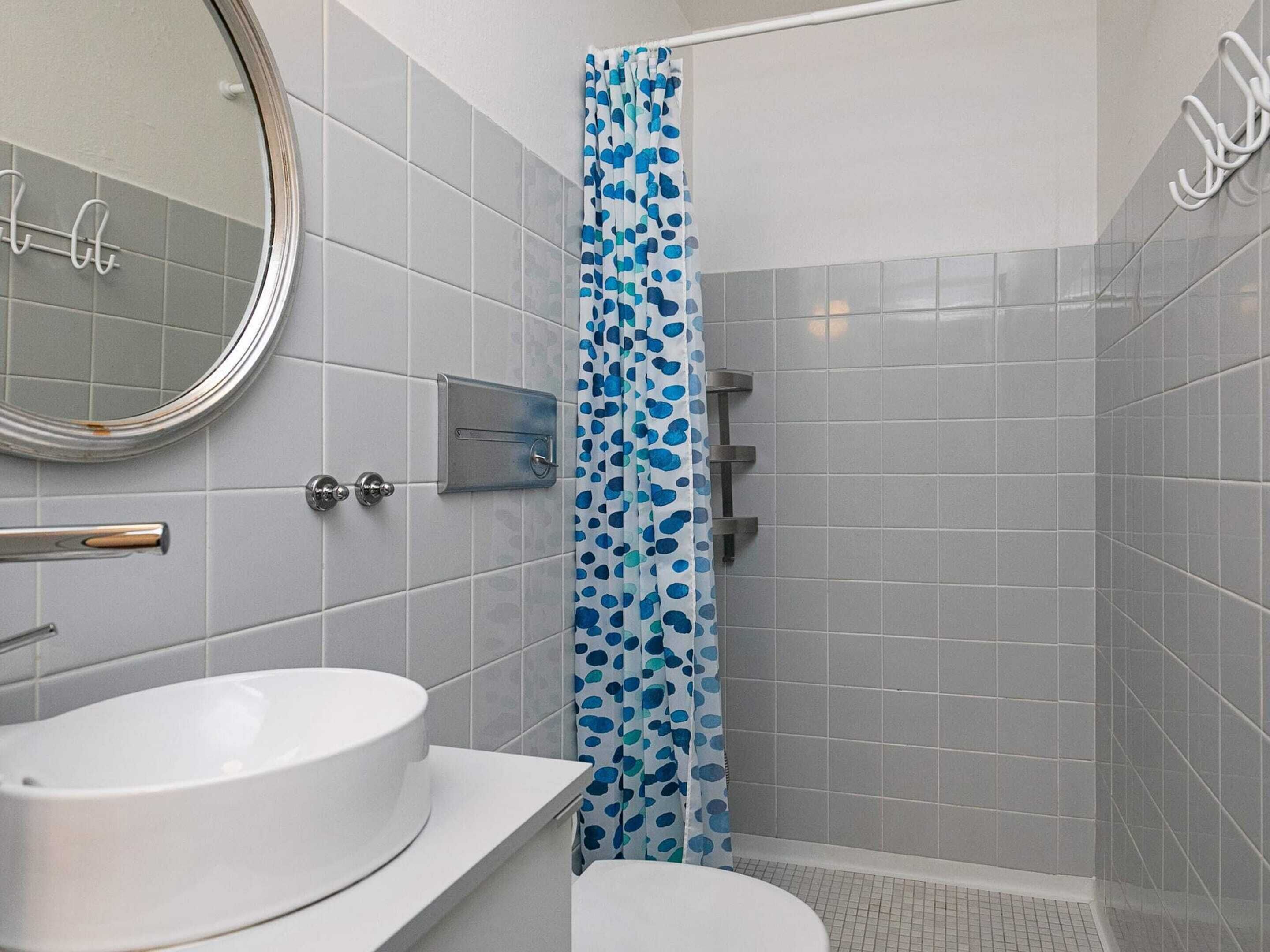 A bathroom with a white sink, a mirror, and a shower with a blue polka dot curtain.