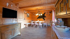 En stuga med träpanel på insidan, med ett matområde, en tv som hänger på väggen och olika jaktpokaler som pryder väggarna.