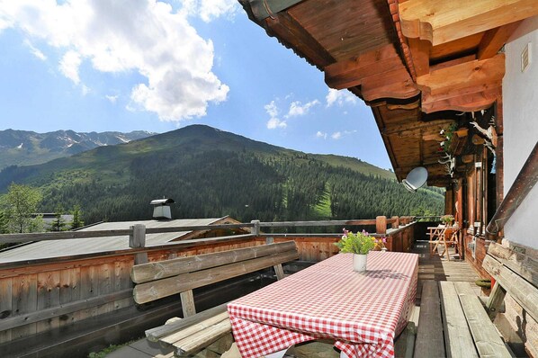 Eine Holzterrasse mit kariertem Tischlein, Holzbänken und Blick auf die Berge.
