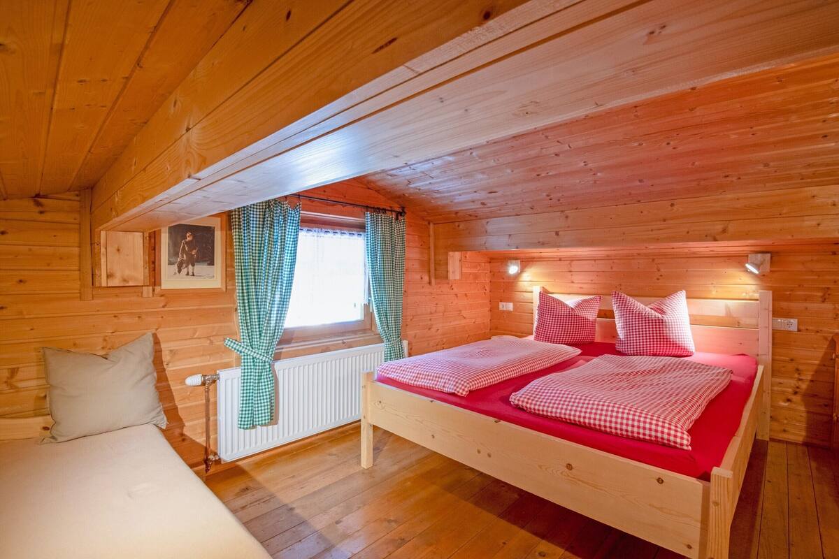 Ein Schlafzimmer in einer Holzhütte mit Bett, Fenster mit Vorhängen und Heizkörper.