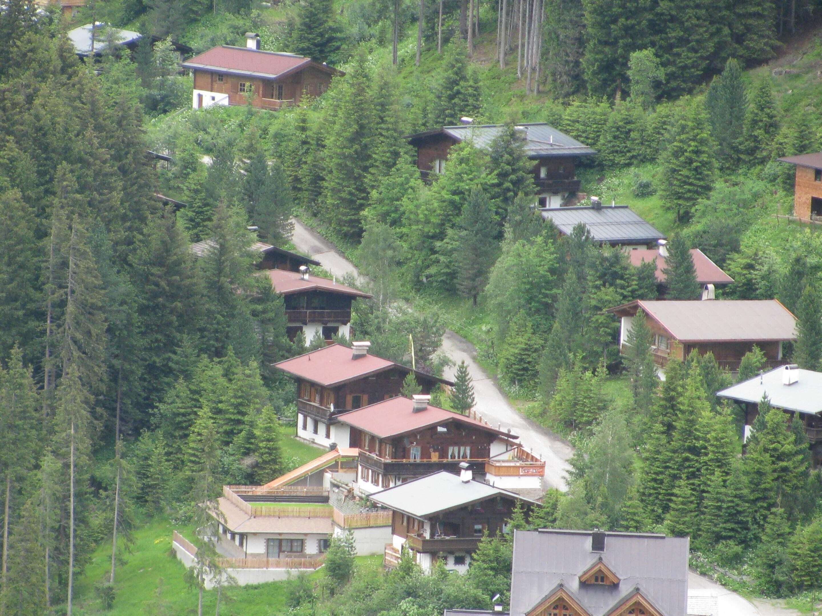 A cluster of wooden cabins surrounded by dense forest, with steep terrain and a winding road.