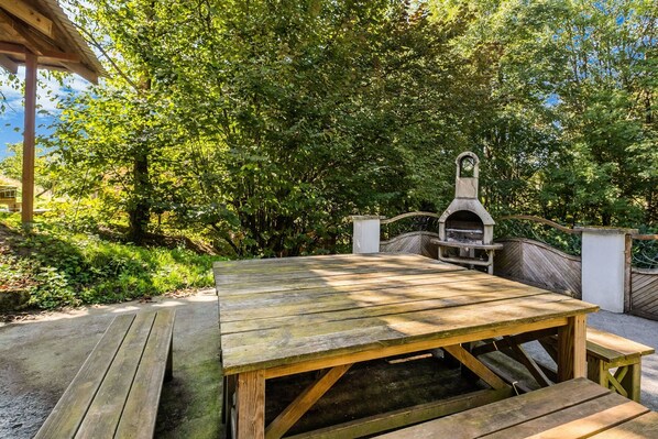 A wooden picnic table with benches, surrounded by lush greenery and a barbecue grill. - Ferienhaus in Willingen Unweit vom Skigebiet (Willingen)