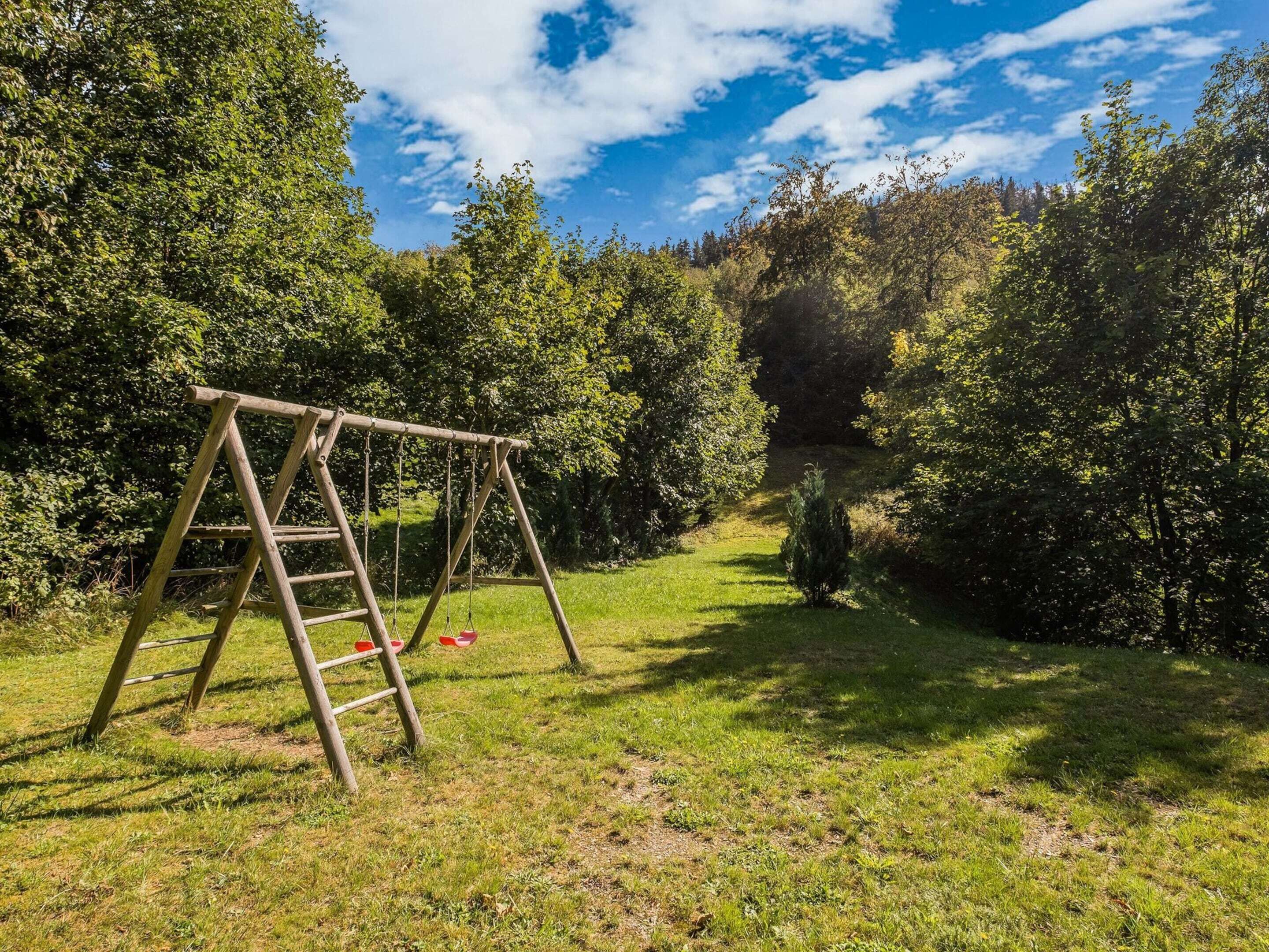 A wooden swing set in a grassy area with trees in the background.