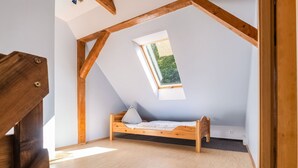 Una habitación pequeña con techo inclinado, una cama individual, un tragaluz y vigas de madera.