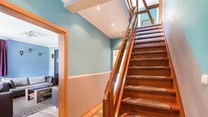 Una escalera que conduce a un piso superior, una sala de estar con sofá y mesa de centro, y una alfombra estampada en el suelo.