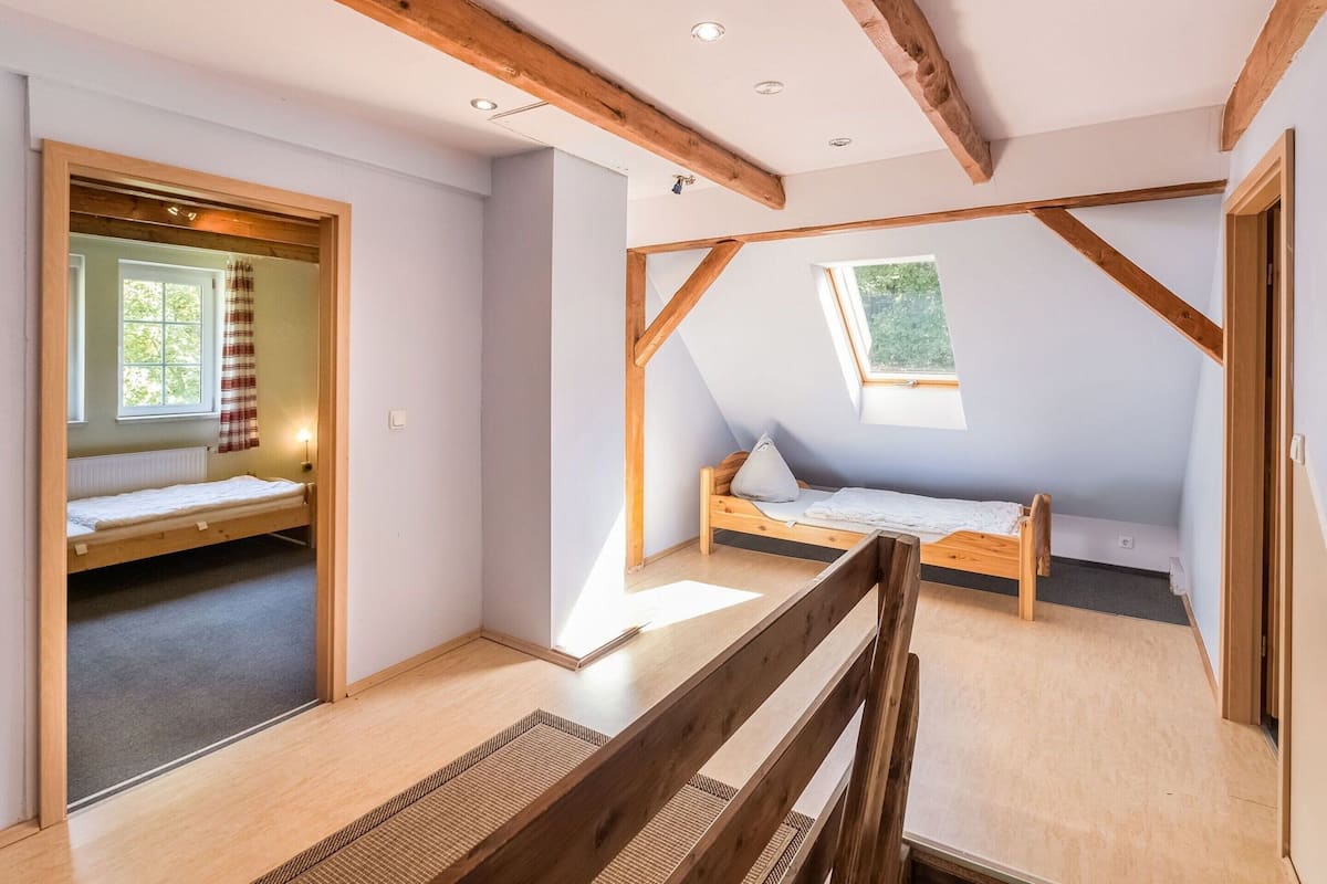 Una habitación con techo inclinado, vigas de madera, dos camas, una ventana y una puerta.