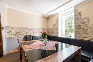 A dining area with a glass table, a vase with flowers, and a stone accent wall. - Ferienhaus in Willingen Unweit vom Skigebiet (Willingen)