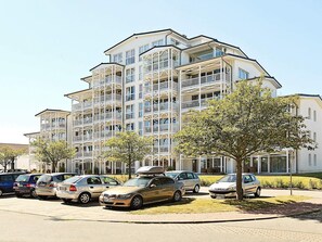 A multi-story residential building with balconies, parked cars, and a tree in the foreground. - 6 Person Holiday Home in Grossenbrode (Grossenbrode)