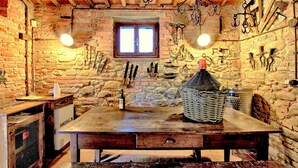 A rustic stone-walled room with a wooden table, hanging tools, and a window. - Comfortable Cottages in Loro Ciuffenna (Terranuova Bracciolini)