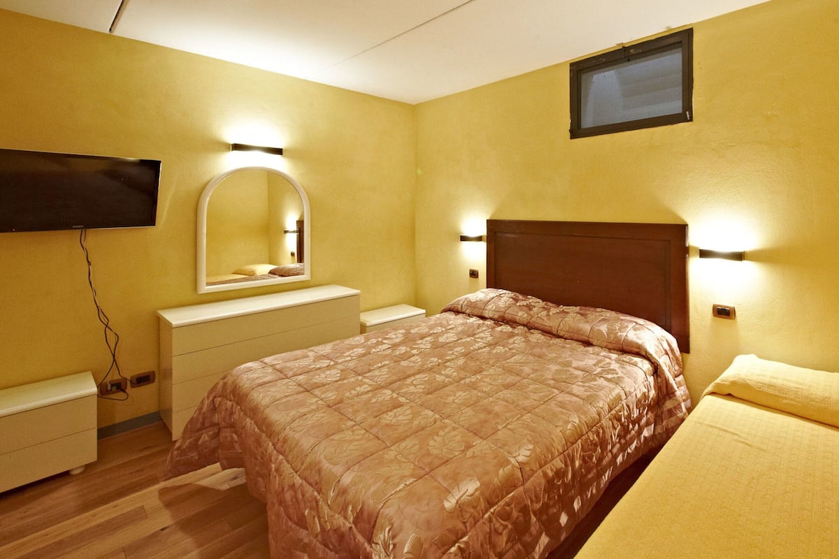 A bedroom with a bed, a dresser, a mirror, and wall-mounted lights.