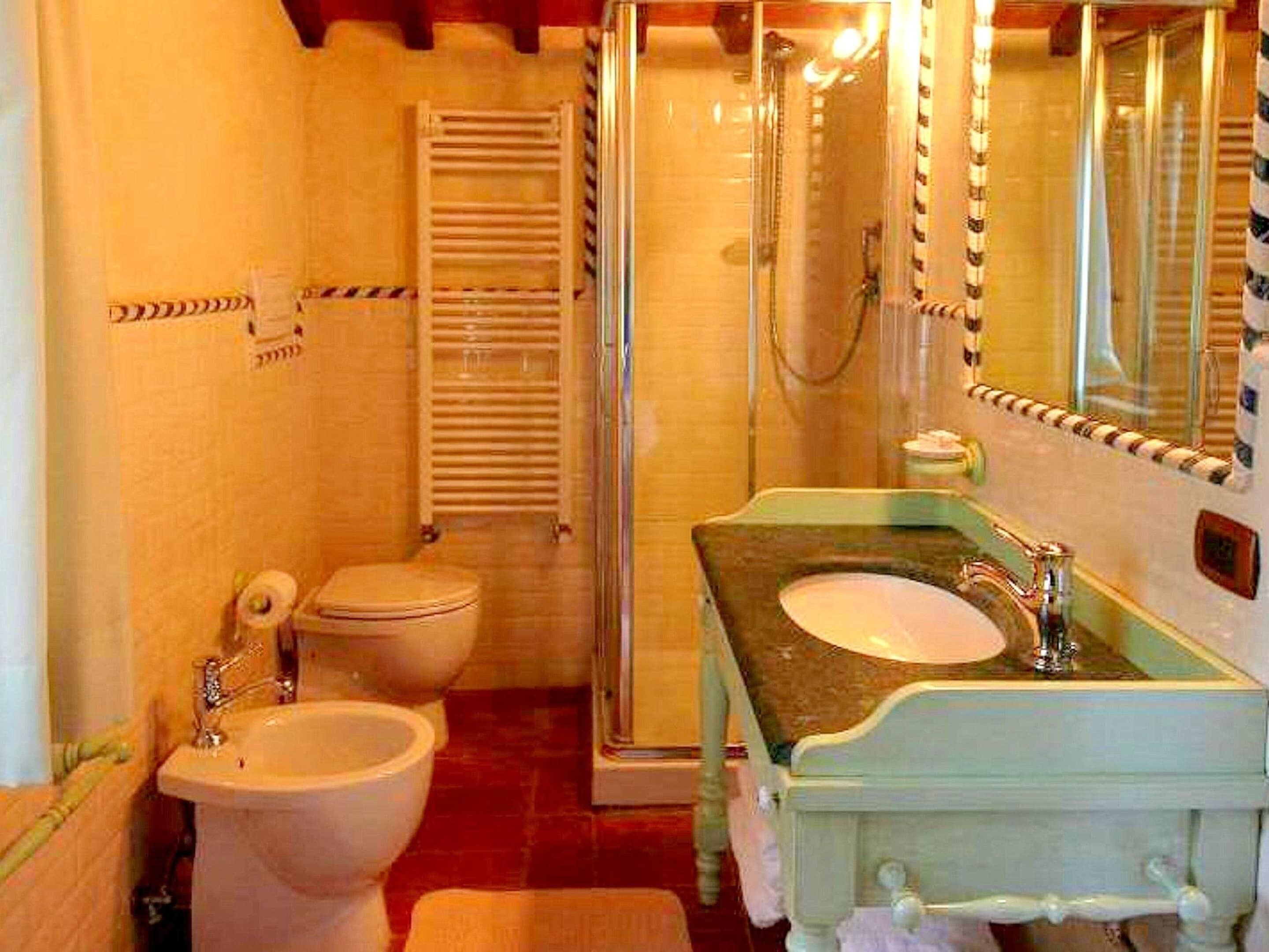 Un bagno con un water bianco, un bidet, una cabina doccia in vetro e un lavabo con specchio.