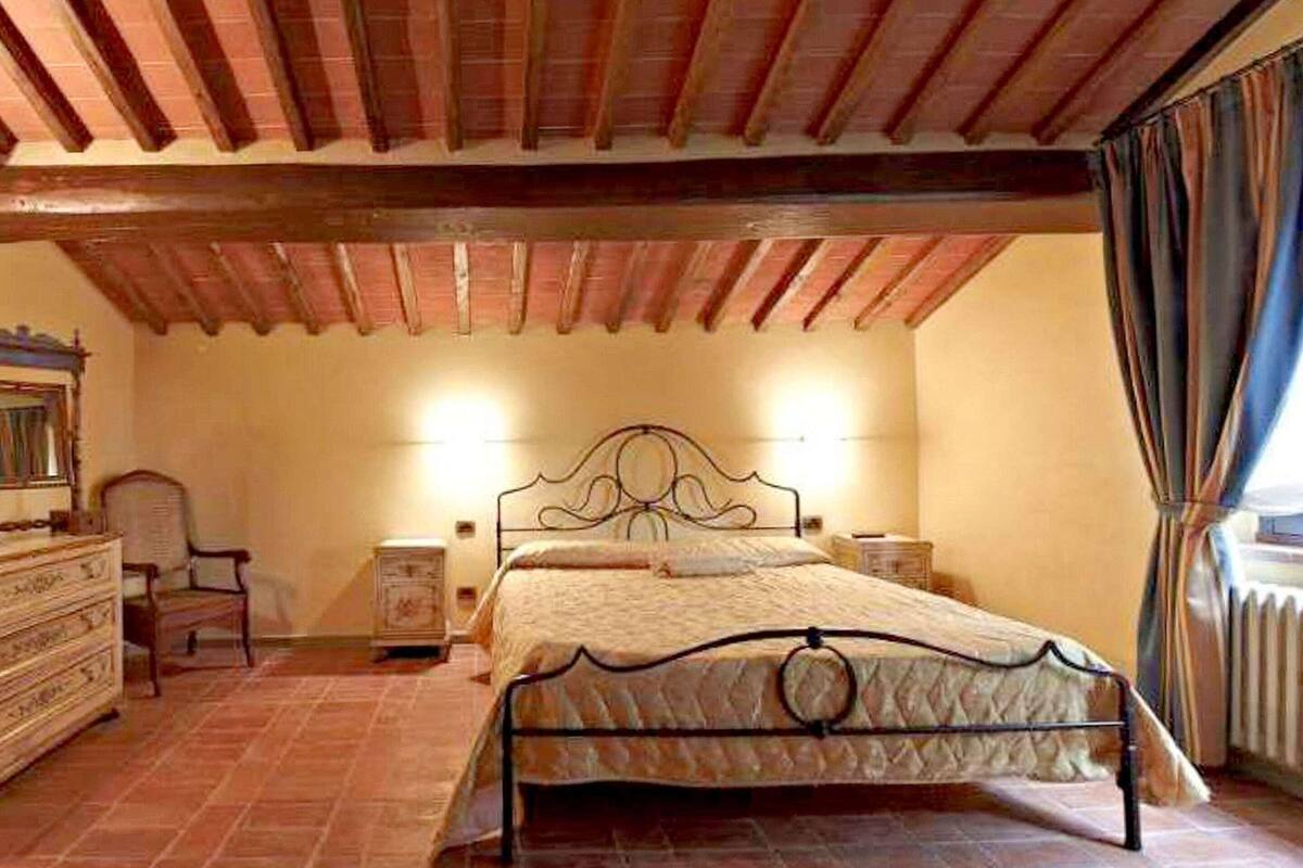A bedroom with a bed, wooden ceiling beams, a dresser, and a nightstand.