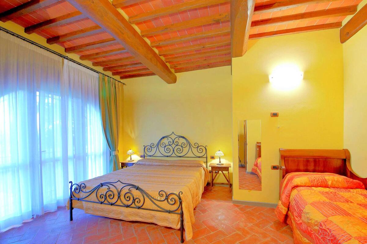 A bedroom with a bed, two bedside tables, a mirror, and a window with curtains.