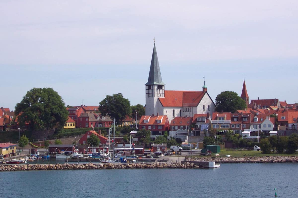 A coastal town with a prominent church steeple, red-roofed buildings, and a marina with boats.