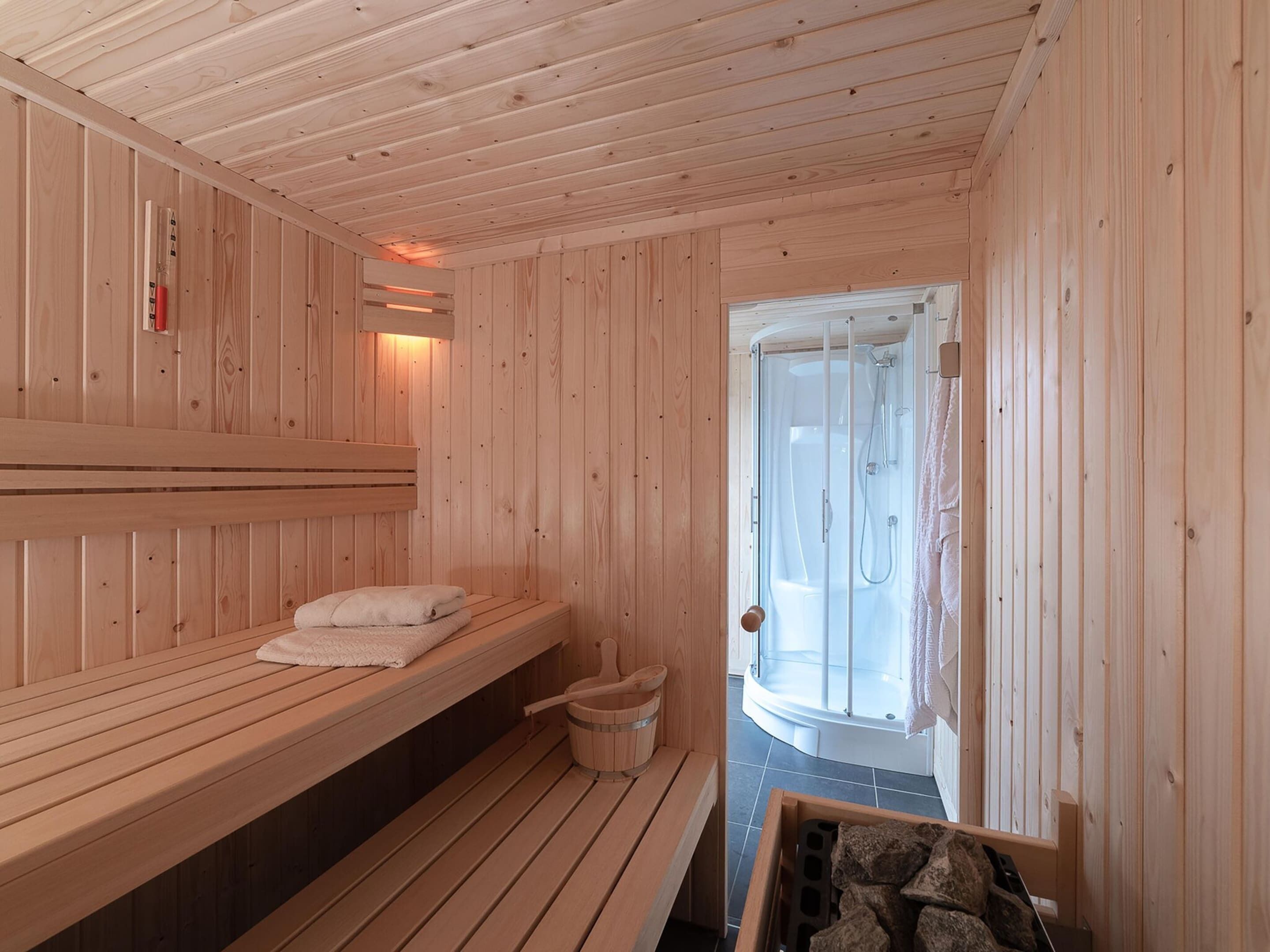 Un cuarto de sauna con bancos de madera y una puerta de vidrio que da a una zona de ducha.