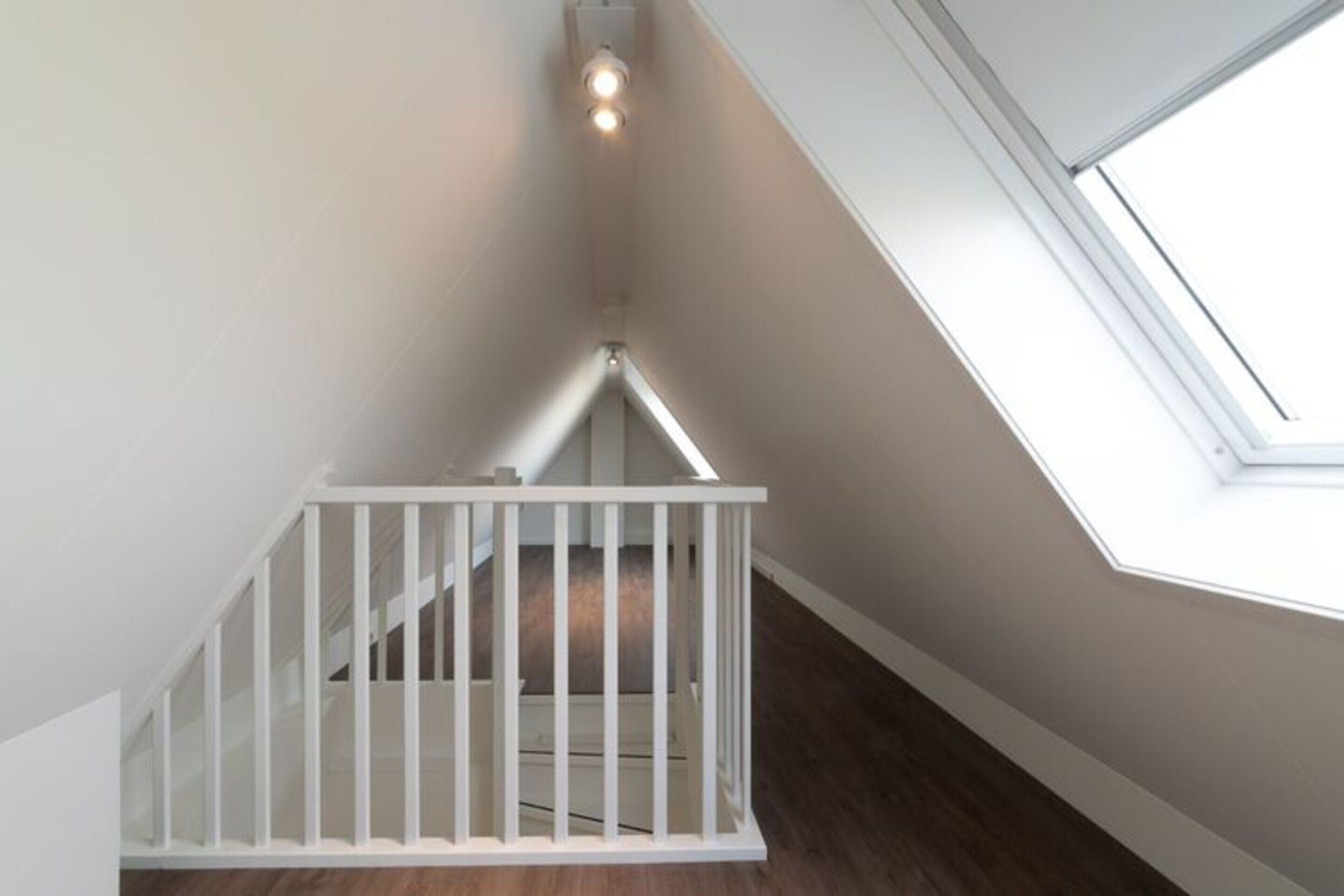 A white crib in a corner with a skylight above.