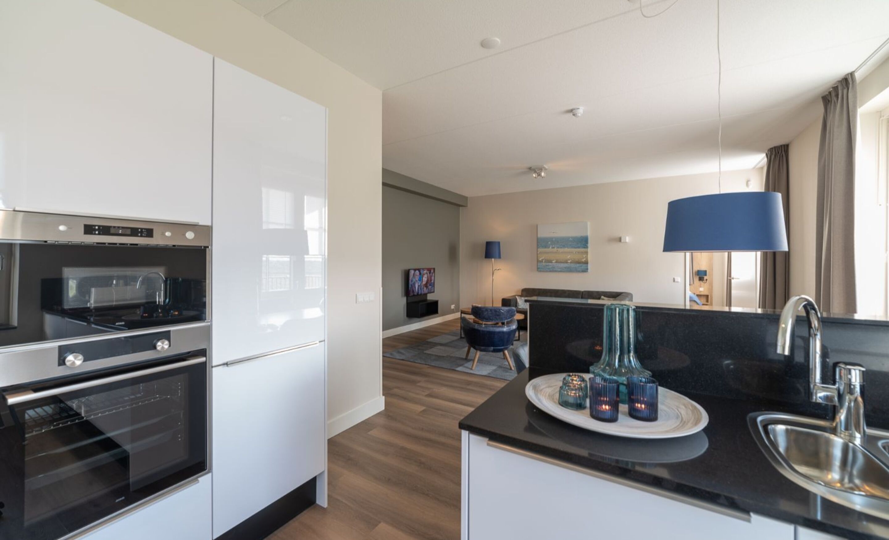A modern kitchen with built-in appliances, a dining area with a table and chairs, and a living room with a sofa and a TV.