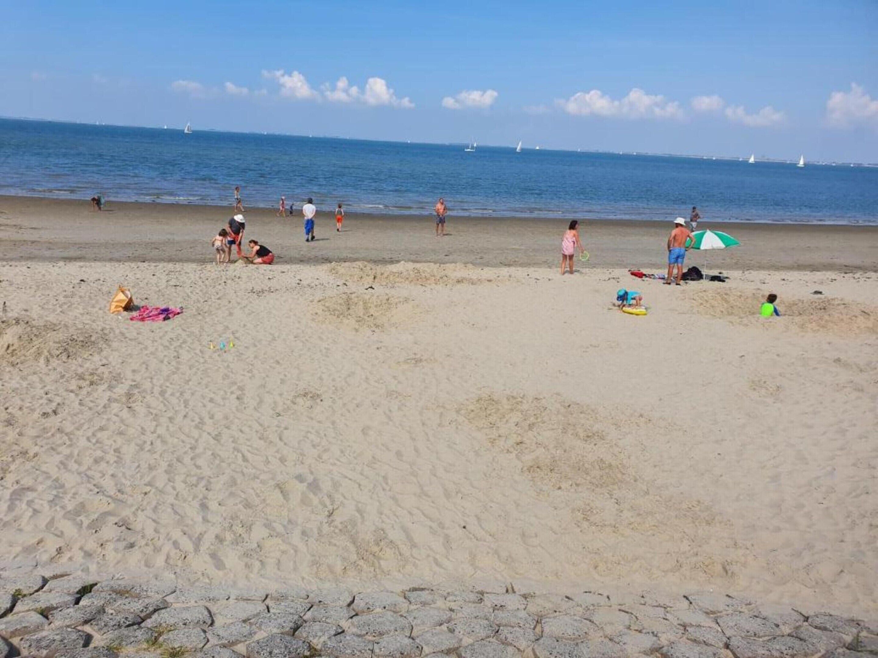 A sandy beach with people, some with umbrellas, and boats in the distance.