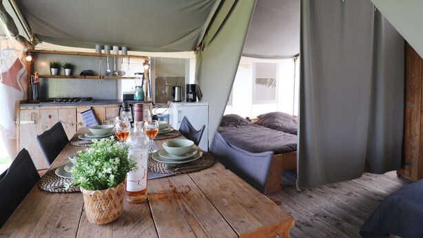 A cozy tented accommodation with a wooden dining table set for two, a kitchenette, and a sleeping area with a bed. - Safari Tent in the Middle of the Fryske Walden (Twijzel)