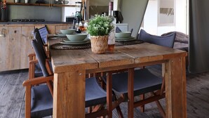A rustic wooden dining table with a woven basket containing a plant and a bottle, surrounded by dark blue upholstered chairs. - Safari Tent in the Middle of the Fryske Walden (Twijzel)