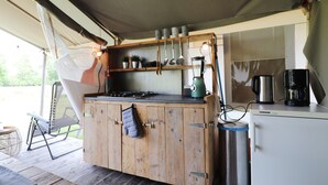 A kitchen with wooden cabinets, a gas stove, a coffee maker, and a refrigerator. - Safari Tent in the Middle of the Fryske Walden (Twijzel)