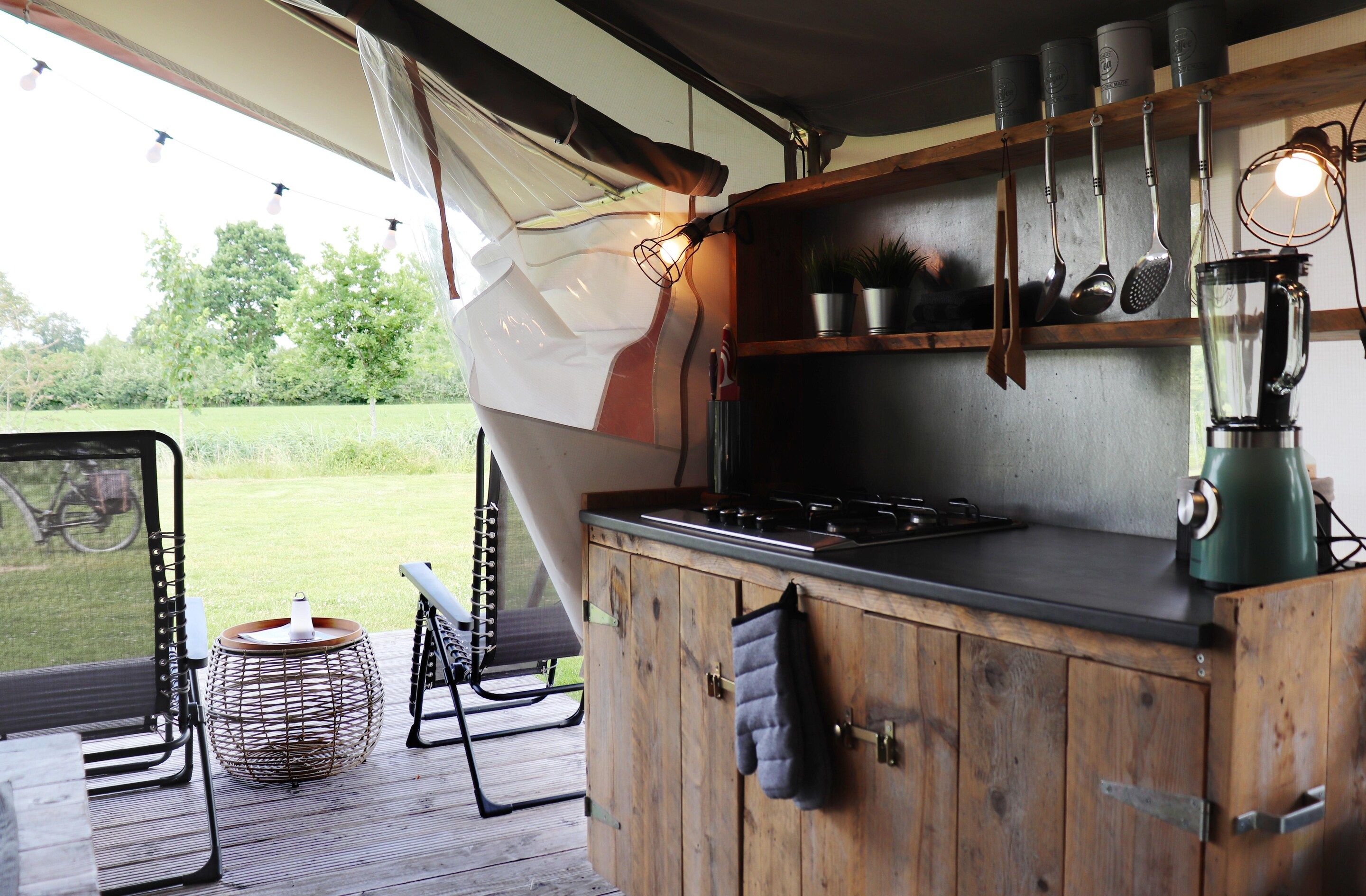 A kitchen with wooden cabinets, a stove, hanging utensils, and a view of the outdoors.