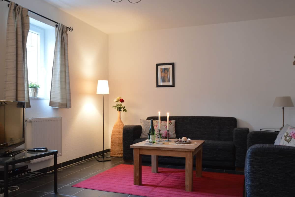 A living room with a dark-colored sofa, a wooden coffee table, a red rug, a floor lamp, and a framed picture on the wall.