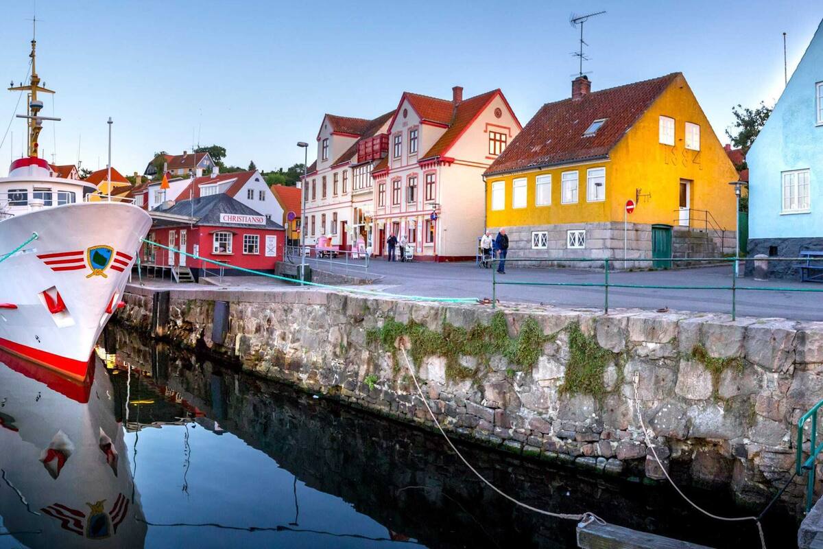 A harbor with boats, a stone wall, and colorful buildings including a red and white building labeled "CHRISTIANSO".