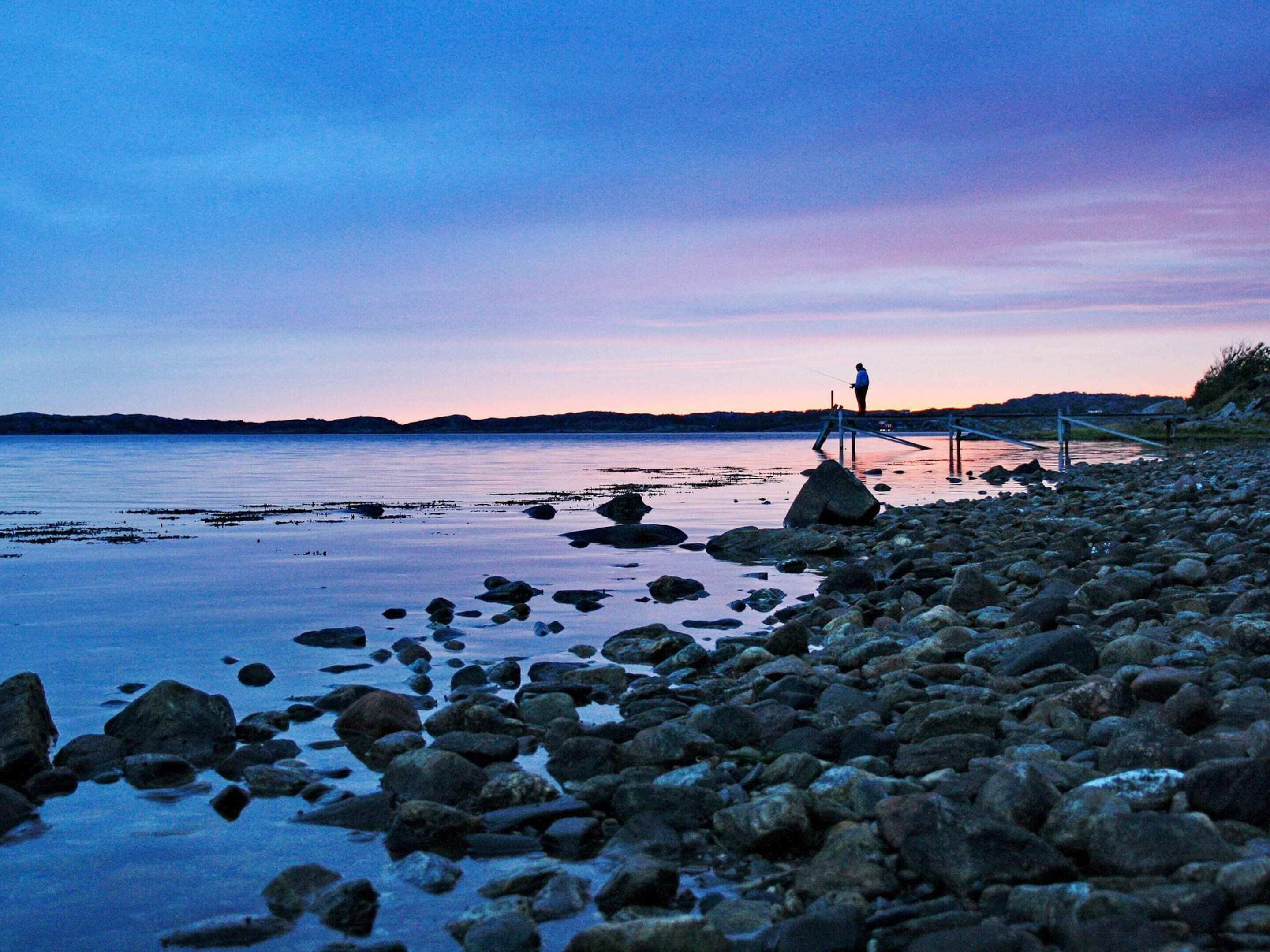 A rocky shoreline with a person fishing at dusk.