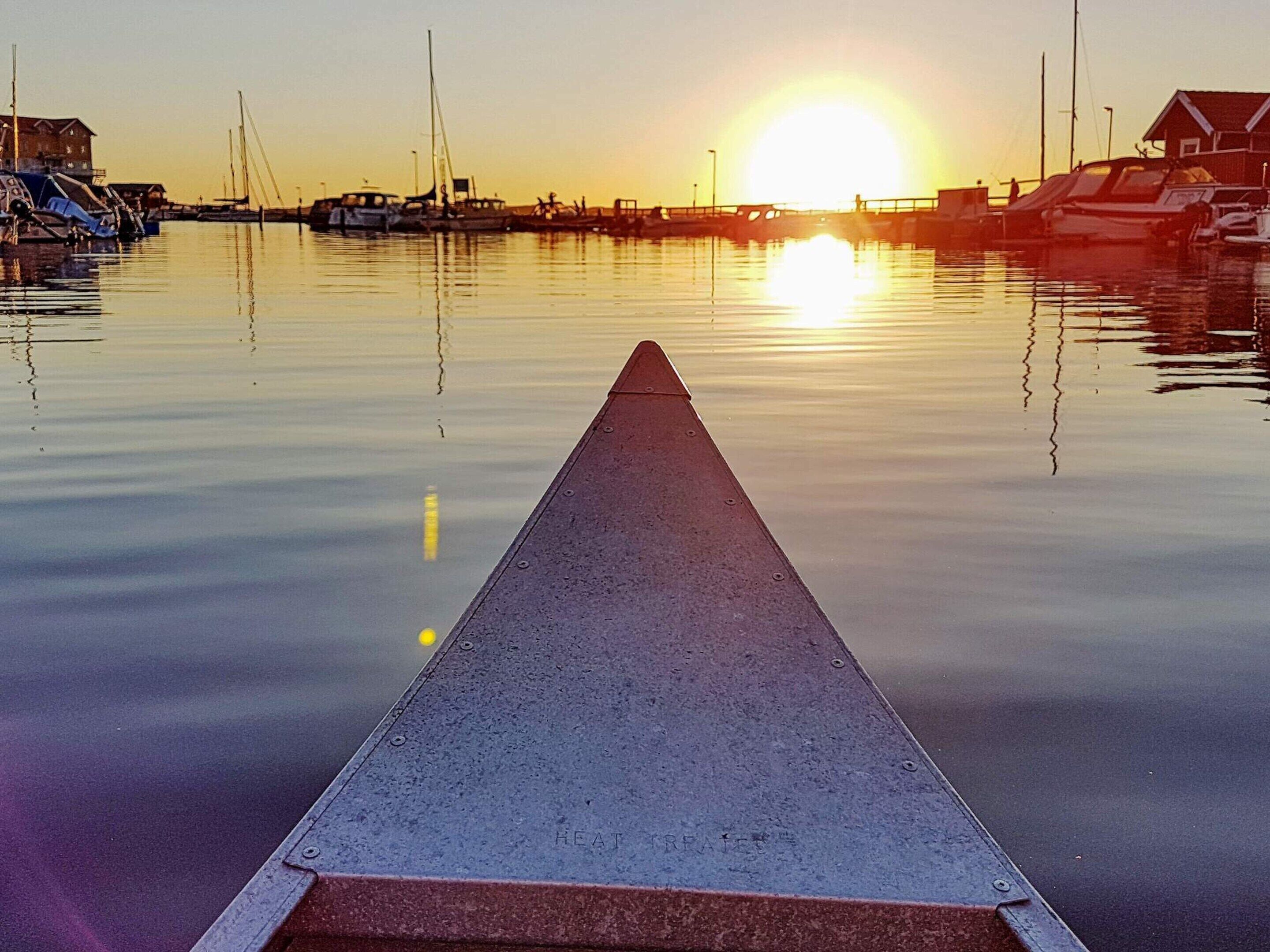 Une jetée menant à une marina, avec des bateaux et des bâtiments en arrière-plan, au coucher du soleil.