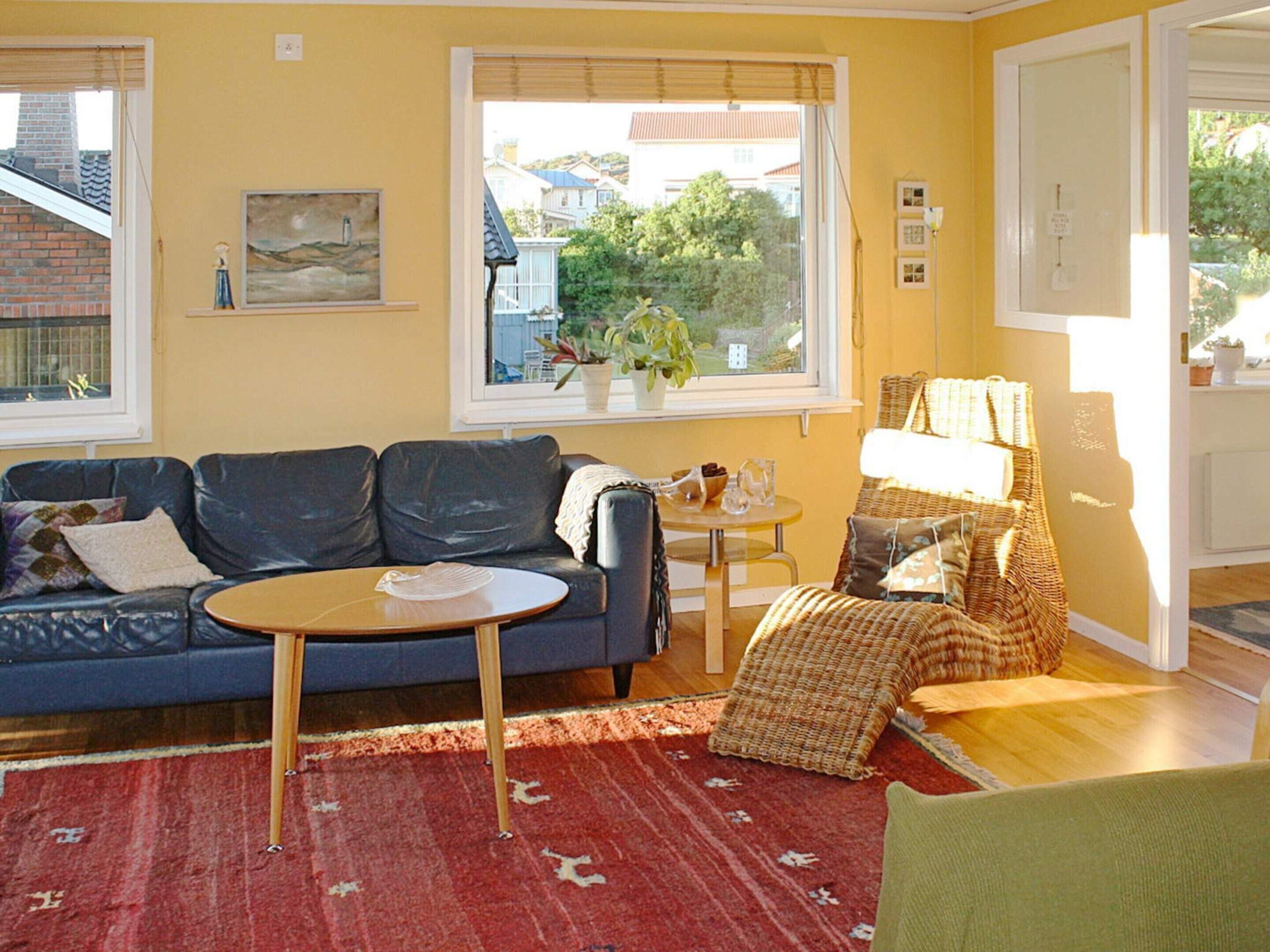 A living room with a blue sofa, a small round table, a red patterned rug, and a view of houses through a window.