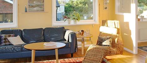 A living room with a blue sofa, a small round table, a red patterned rug, and a view of houses through a window.