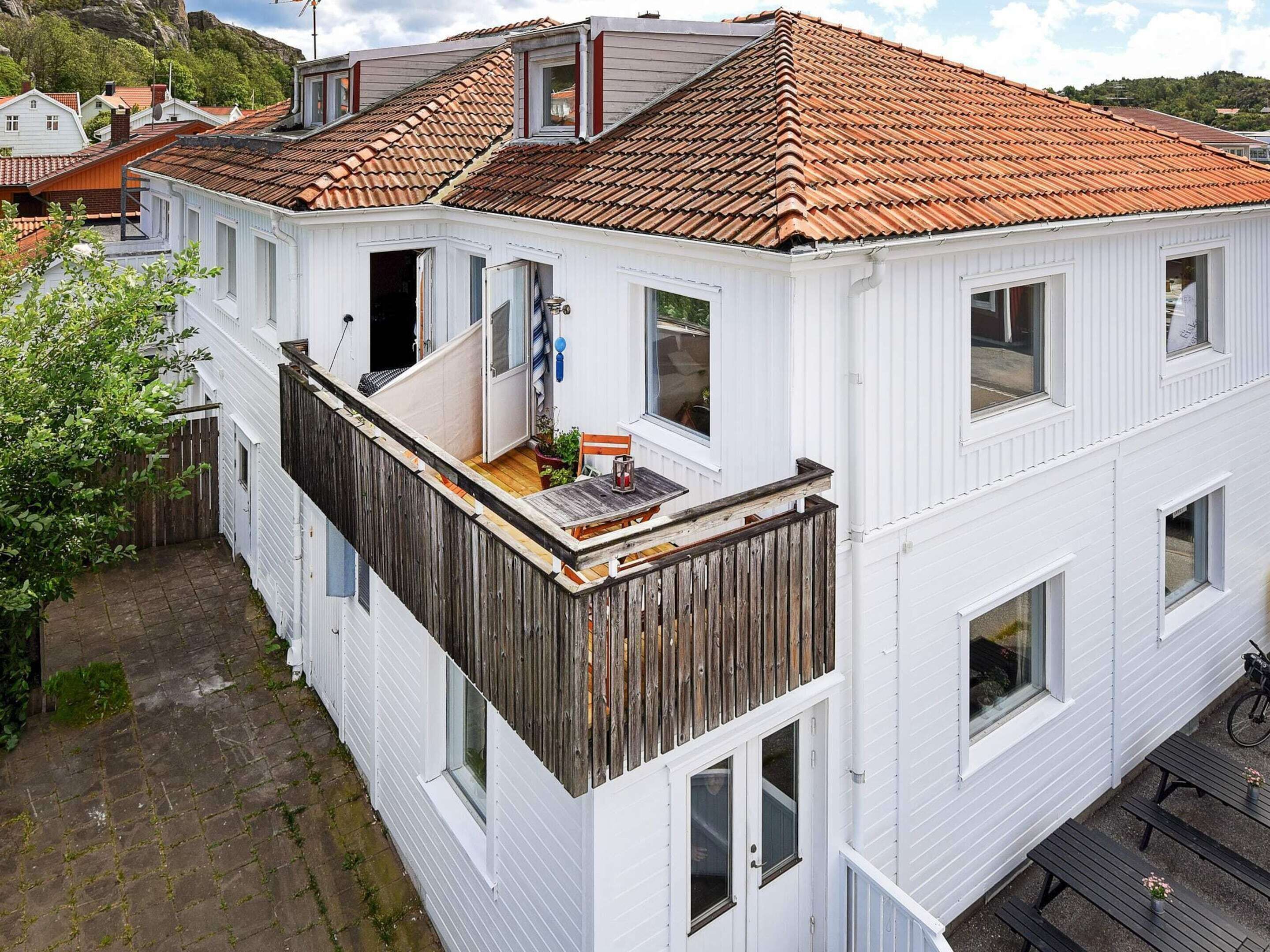 A white two-story house with a red-tiled roof, a wooden balcony, and a small garden area.